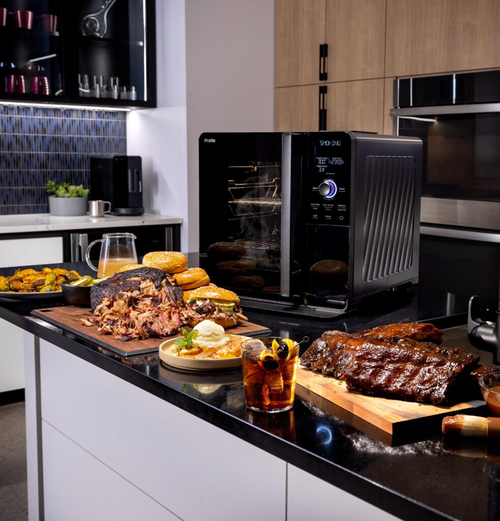 GE Profile Smart Indoor Smoker in use with a variety of foods prepared on a kitchen counter.