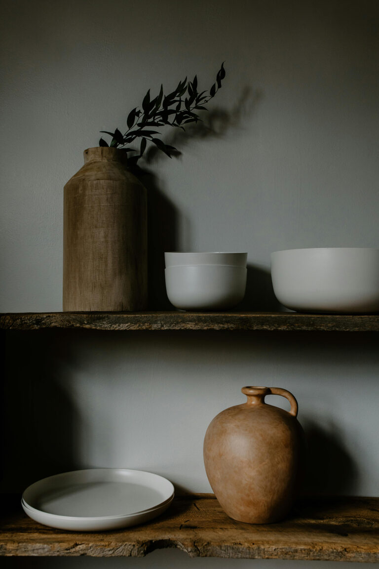 Japandi-inspired shelf decor with a rustic wooden vase, minimalist white bowls, and a clay jug against a neutral backdrop.