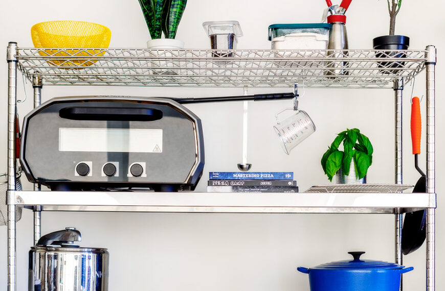 Organized vertical kitchen shelving unit with cooking tools, appliances, and fresh ingredients in a small urban kitchen.